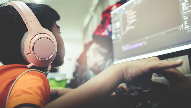 Asian kid is coding and scripting program on on his game streaming desktop computer with headphone on.