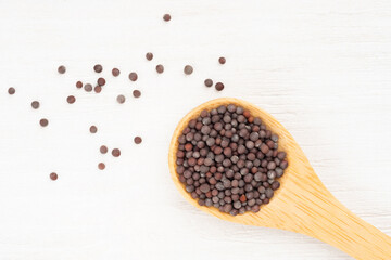 Mustard seeds in wooden spoon and scattered on white wooden background. Close up. Vegetarian food concept
