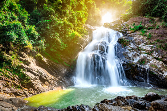 Beautiful Waterfall At The Mountain With Blue Sky And White Cumulus Clouds. Waterfall In Tropical Green Tree Forest. Waterfall Is Flowing In Jungle. Nature Abstract Background. Granite Rock Mountain.