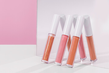 Three different shades of lip gloss are leaning up against a mirror. There is a pink background and...