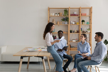 Team of ambitious millennial corporate staff members communicate in office during morning briefing lead by young Hispanic lady. Team-work, teambuilding, workflow of four multi racial employees concept