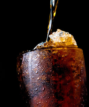 Soft drink pouring to glass with ice isolated on dark background with clipping path and copy space. There is a drop of water on the transparent glass surface.