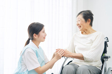 室内で車椅子に乗る高齢者女性と笑顔で会話する介護士