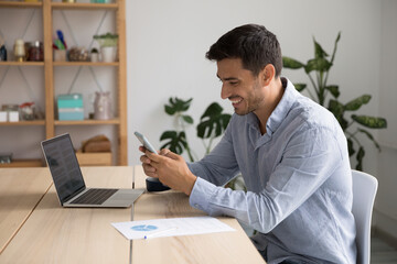 Smiling 35s Hispanic businessman, office employee hold cellphone sit at workplace, check e-mail app, usage of mobile business application, comfort easy life use modern wireless tech at work concept