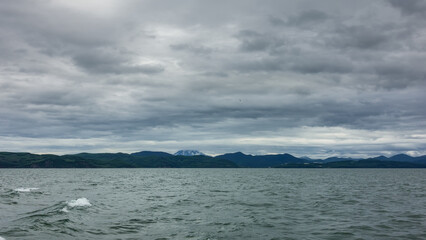 Ripples and waves on the surface of the Pacific Ocean. In the distance, against the background of a cloudy sky - a mountain range. The volcano is hiding in the clouds. Kamchatka. Avacha Bay