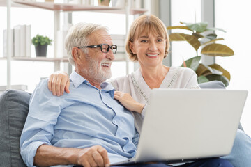 Fototapeta premium Happy senior couple, elderly family, caucasians mature, adult lover and retired man, woman using laptop computer shopping online, reading news on sofa at home together. Husband and wife lifestyle.