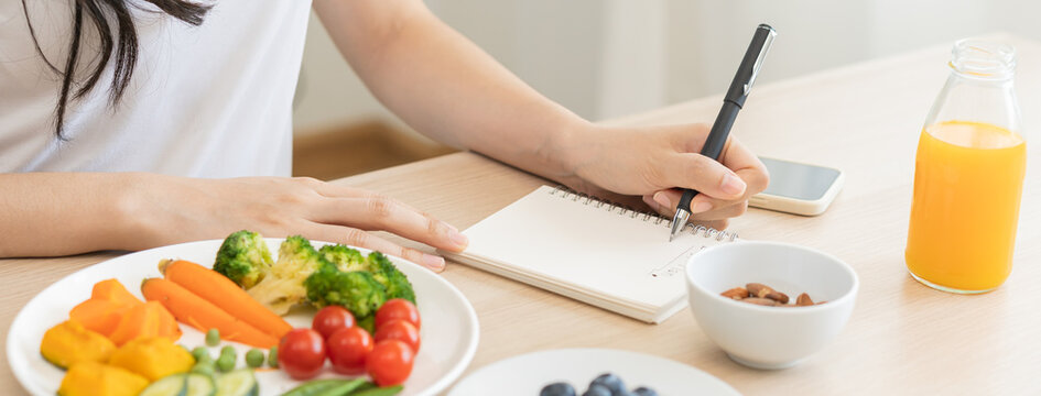 Diet, Dieting Hand Of Woman Write Diet Plan Right Nutrition On Table With Fresh Vegetables Salad, Almond Is Different Food Ingredients In The Green. Nutritionist Of Healthy, Nutrition Of Weight Loss.