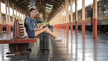 Young woman waving hand while sitting at railroad station platform.