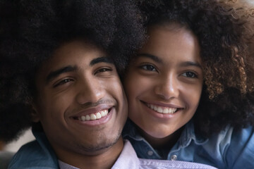 Close up happy faces beautiful African 18s girlfriend hugging piggyback boyfriend posing look aside. Portrait of brother and sister, family bond. Affectionate couple, first love, relationship concept