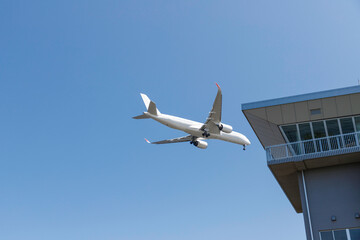 青空を背景に管制塔の上を着陸態勢に入る飛行機