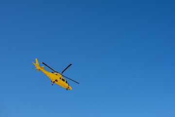 Yellow rescue helicopter taking flight on a blue background. Image with copy space