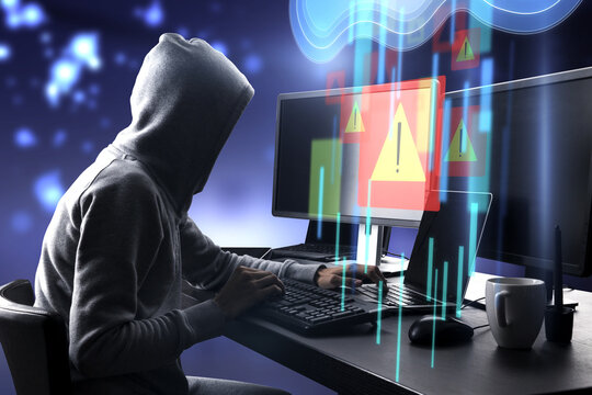 Warning system and cyber attack concept with side view on hacker in hoody working on computers and virtual data cloud network interface with exclamation point