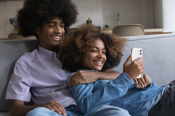 Teenage 18s girl and guy relax together on sofa have fun use mobile app on cellphone. Couple ordering food through e-services for easy comfort life, young generation and wireless tech usage concept