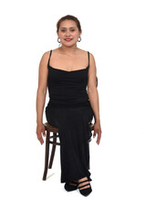 front view of a woman with dress and heeled shoes sitting on chair ,smiling and looking at camera...