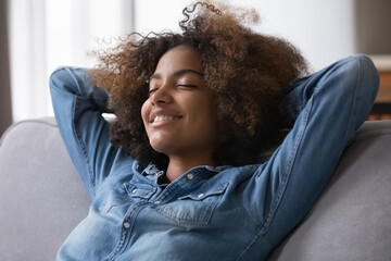 Fototapeta premium Close up beautiful peaceful African teenage girl relaxing alone at modern home breathing fresh conditioned air in cozy warm living room. Enjoy stress free weekend, repose, healthy daytime nap concept