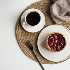 Morning breakfast with coffee and berry pie. Aesthetic still life composition with dessert, coffee, flowers bouquet, linen blanket, fork on white table. Flat lay, top view