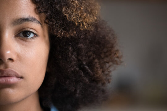 Close up cropped half non-make up face view of young 20s gorgeous African beautiful girl pose look at camera. American serious cute curly-haired teenager portrait, gen Z person, natural beauty concept
