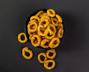 Traditional Indian snack arranged beautifully in a black ceramic bowl with a black textured background. It is known as Chakali, Murukku, Muruku, Murkoo, Chakri. Top view.