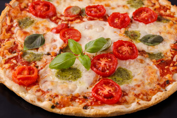 Baked vegetarian crusty pizza with mozzarella, cherry tomatoes, pesto sauce and basil leaves closeup