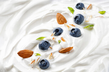 Background Yogurt with blueberry, almond and mint. Tasty liquid Texture of white sour cream, ice cream with blueberry. Creamy dairy product.