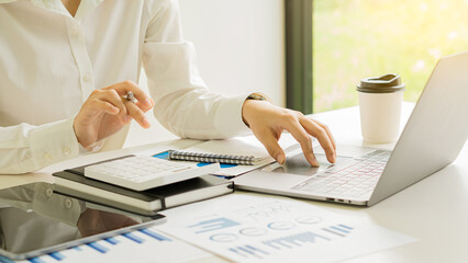 Asian businessman hand pressing calculator and preparing data while using clamp to analyze investment advisor chart. and auditors to calculate costs with a laptop at the desk in the office.