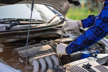 Fototapeta na wymiar Asian man standing in front of inspection vehicle and inspecting machinery Problems in the car engine in the house and found problems inside the car to repair. Asian man maintains a car's engine