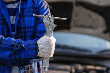 A mechanic with a wrench in his hand stood in front of the car to fix the car's engine problem. Concept of car inspection and repair and maintenance services