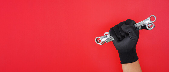 hand wearing black gloves holding  different size box end wrench isolated red background