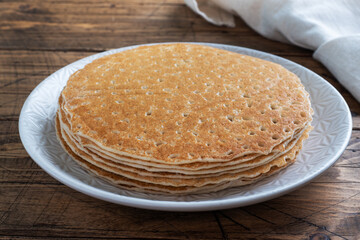 Thin pancakes on a plate, top view, wooden background. The concept of a delicious breakfast or Maslenitsa.