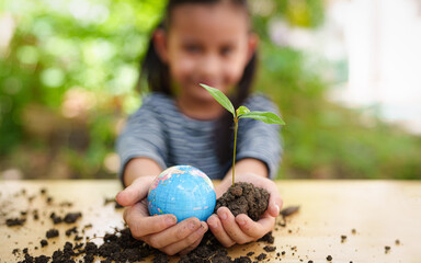Blurred of little girl is holding plant and globe model together, concept of ESG, environment, earth day, sustainability, world environment day, montessori education for kid and home school.