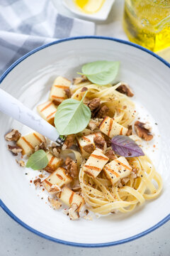Close-up of creamy pasta with chopped grilled halloumi and walnuts in a white plate, vertical shot, selective focus