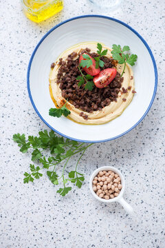 White plate with hummus and ground beef on a beige granite background, vertical shot, view from above