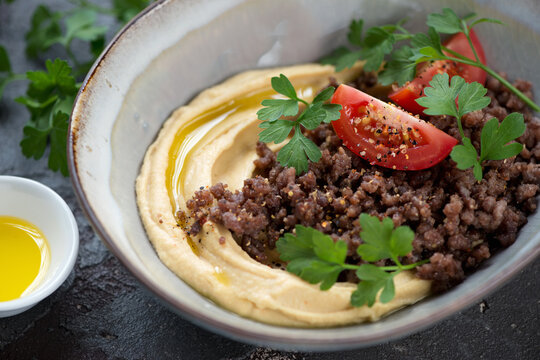 Closeup of hummus served with ground beef meat and fresh parsley in a grey bowl, selective focus