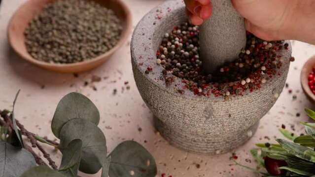 Men's hands grind mixed whole pepper berries in a mortar