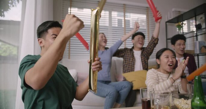 Group of young adult friend man and woman asia people sit at sofa couch joy chanting party fun game FIFA world cup live TV at home eat snack bowl drink beer bottle glass jump mad happy win exult face.