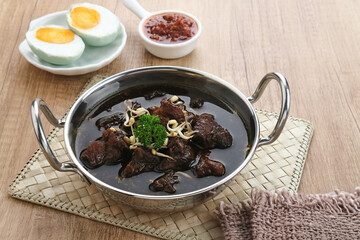 Rawon, Indonesian Traditional beef black soup. Served on a bowl with mung bean sprouts, chilli paste and salted egg
