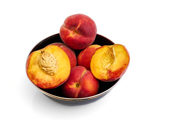 halves and whole juicy peaches in a black bowl on a white background