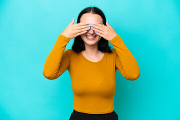 Young caucasian woman isolated on blue background covering eyes by hands and smiling