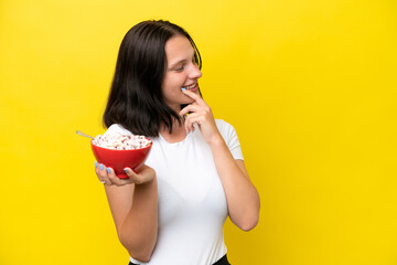 Young caucasian woman holding a bowl of cereals isolated on yellow background thinking an idea and looking side