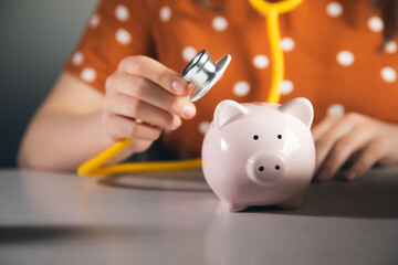 woman listens to a piggy bank with a stethoscope