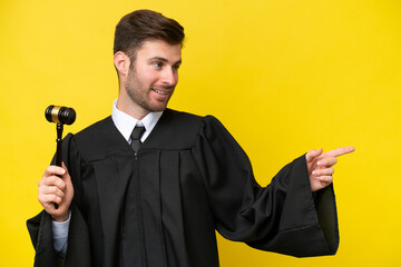 Judge caucasian man isolated on yellow background pointing finger to the side and presenting a...
