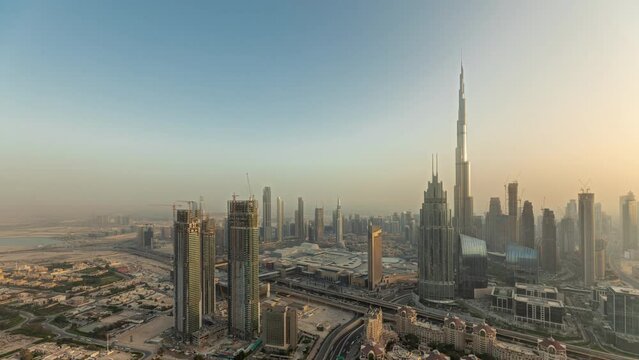 Panorama showing aerial view of tallest towers in Dubai Downtown skyline and highway timelapse before sunset. Financial district and business area in smart urban city. Skyscraper and high-rise