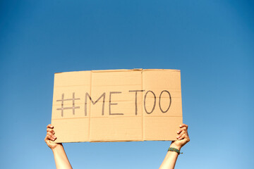 Two woman's hands holding a cardboard sign that says me too No sexism concept.