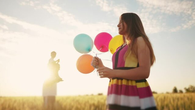 happy family on holiday in the park with balloons. father wears his son playing in a field with wheat in nature in the park. girl with balloons kid concept. friendly family at a birthday party dream