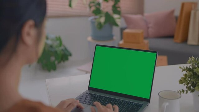 Over the shoulder shot of a business woman working in office interior on pc on desk, looking at green screen. Office person using laptop computer with laptop green screen.