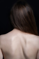Fototapeta premium Beauty and fashion concept. Beautiful wild looking woman with naked back standing in front of camera. Model with long brown hair and smooth skin. Studio shot in black background with copy space