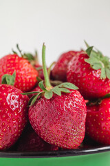 Fresh red strawberry close up in a green enamel bowl on a white background.