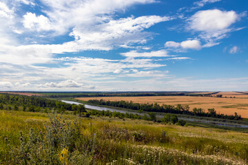 Summer, landscape with a view of the meadow, fields, river and blue sky. Sunny summer scene with river, fields, green hills and beautiful clouds in the blue sky. Nice panoramic view.