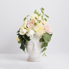 Fresh bunch of colorful flowers in human head shaped vase on grey background. Summer composition. Interior wall or table decoration. Minimal style.