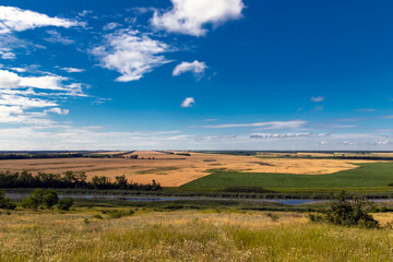 Obraz premium Sunny summer landscape with a river. Green hills and meadows. Fields of ripe wheat.